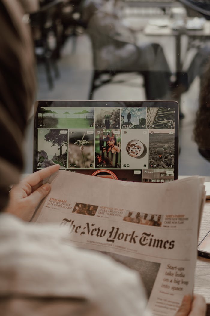 Woman reading The New York Times with a laptop displaying images in a café setting.
