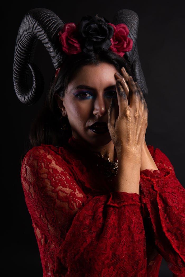 Striking portrait featuring a model with horns, gold hands, and a red dress on a black background.