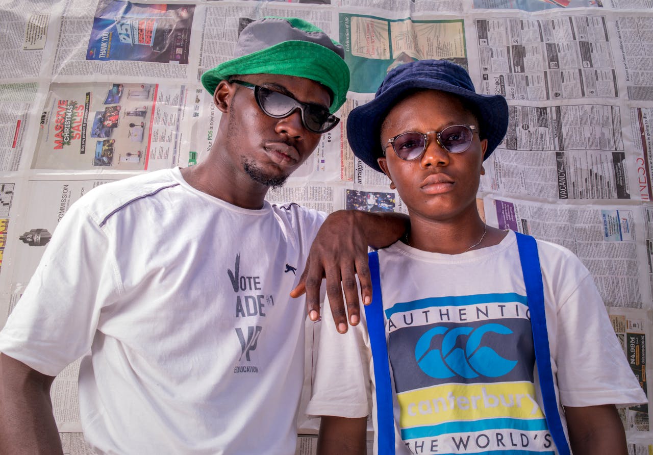 Fashionable photo of two men in sunglasses and hats, posing confidently against a newspaper backdrop in Nigeria.