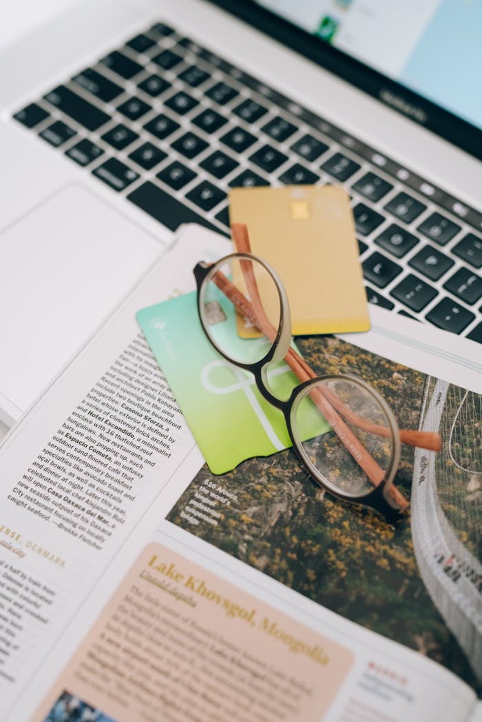 Close-up view of a laptop, credit cards, and eyeglasses on newspaper for a modern work setting.
