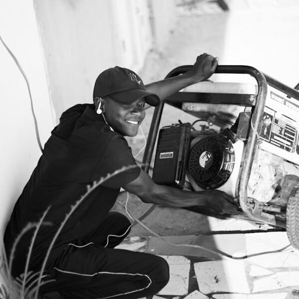 A cheerful young man wearing a cap and earphones operating a portable generator outside.