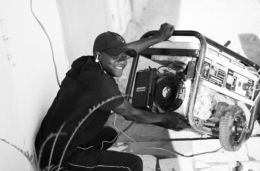A cheerful young man wearing a cap and earphones operating a portable generator outside.