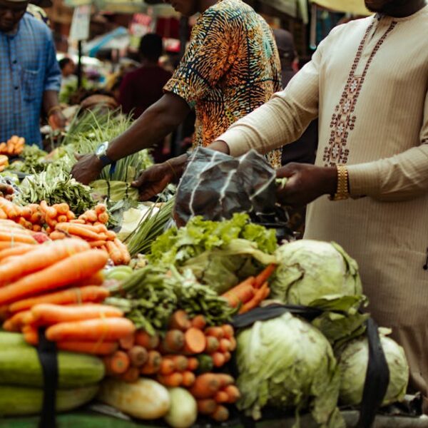 Bustling market scene with fresh vegetables and shoppers in colorful clothing.