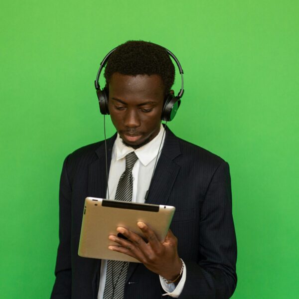 Focused businessman in suit using a tablet with headphones, isolated on a vibrant green background.