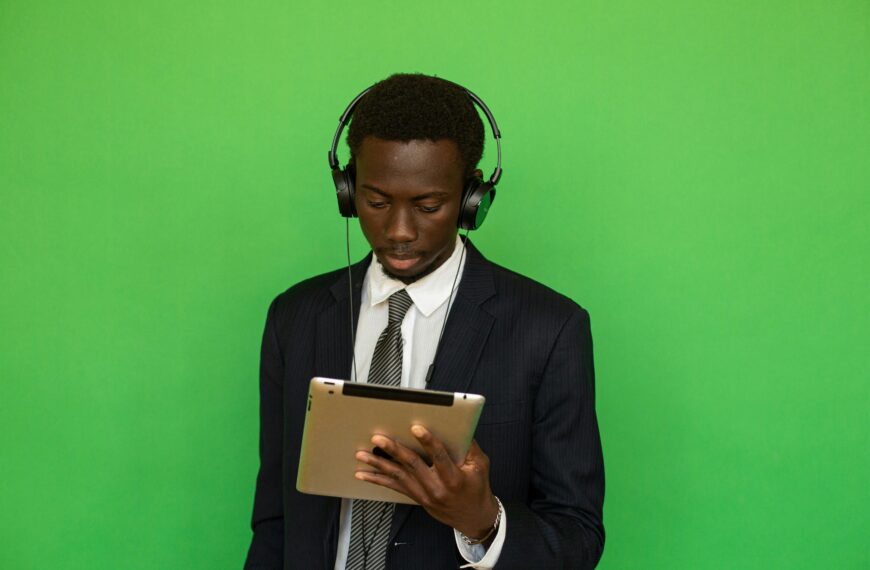 Focused businessman in suit using a tablet with headphones, isolated on a vibrant green background.